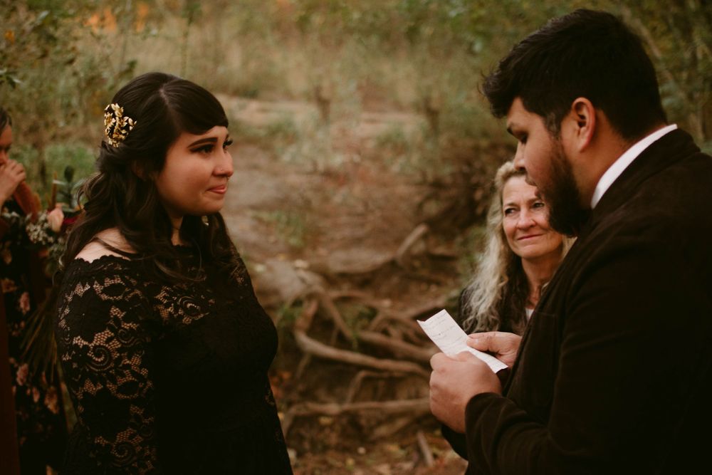 Intimate forest wedding ceremony with couple and officiant reading vows at sunset.