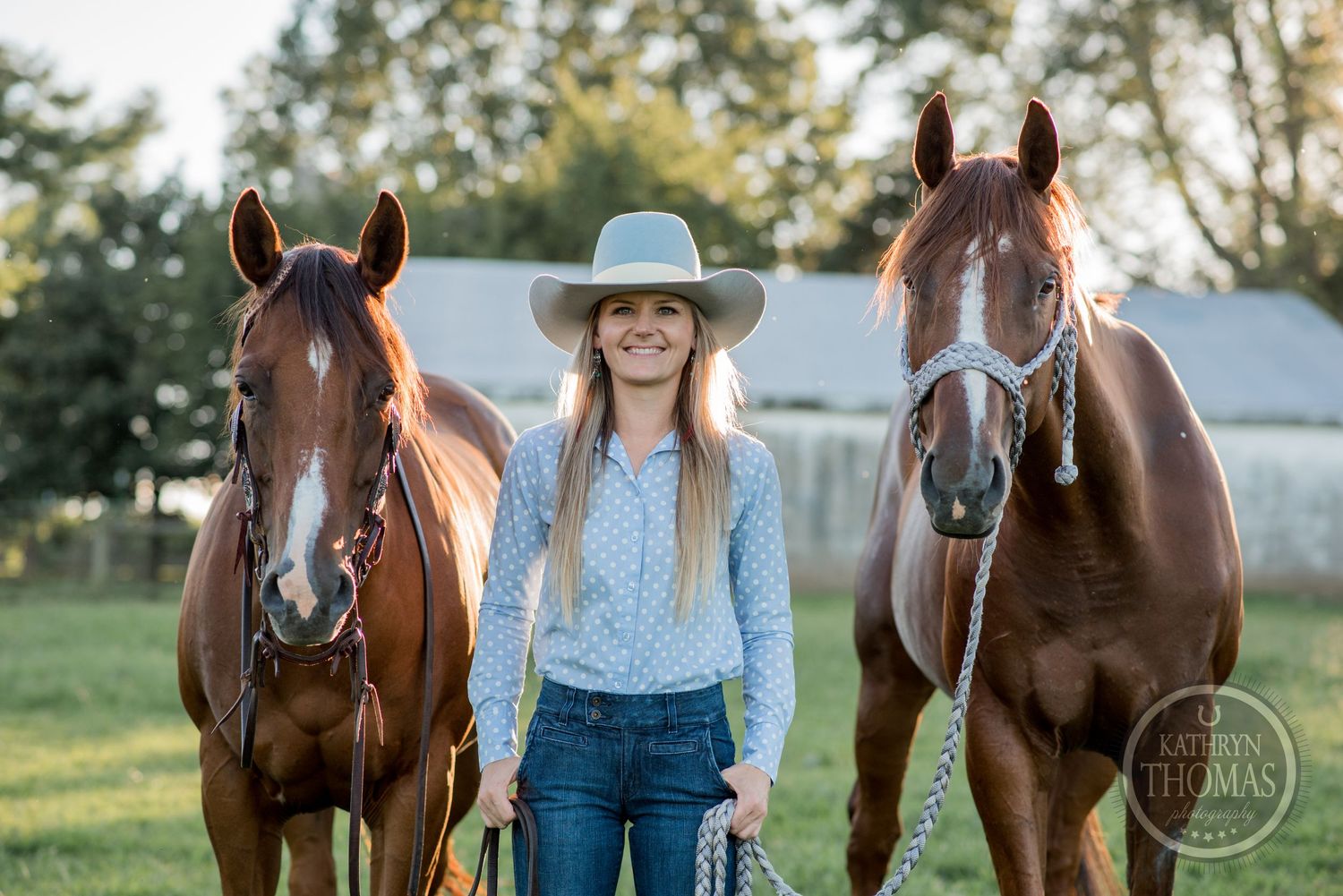 A sunny outdoor portrait with a person in a cowboy hat standing between two majestic brown horses.
