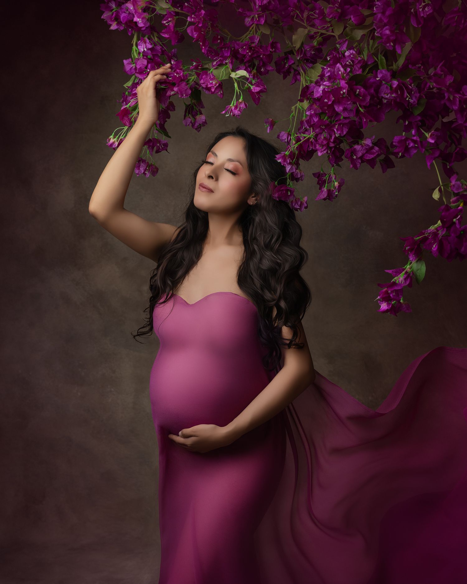 Elegant maternity portrait with flowing purple dress and vibrant magenta flowers.