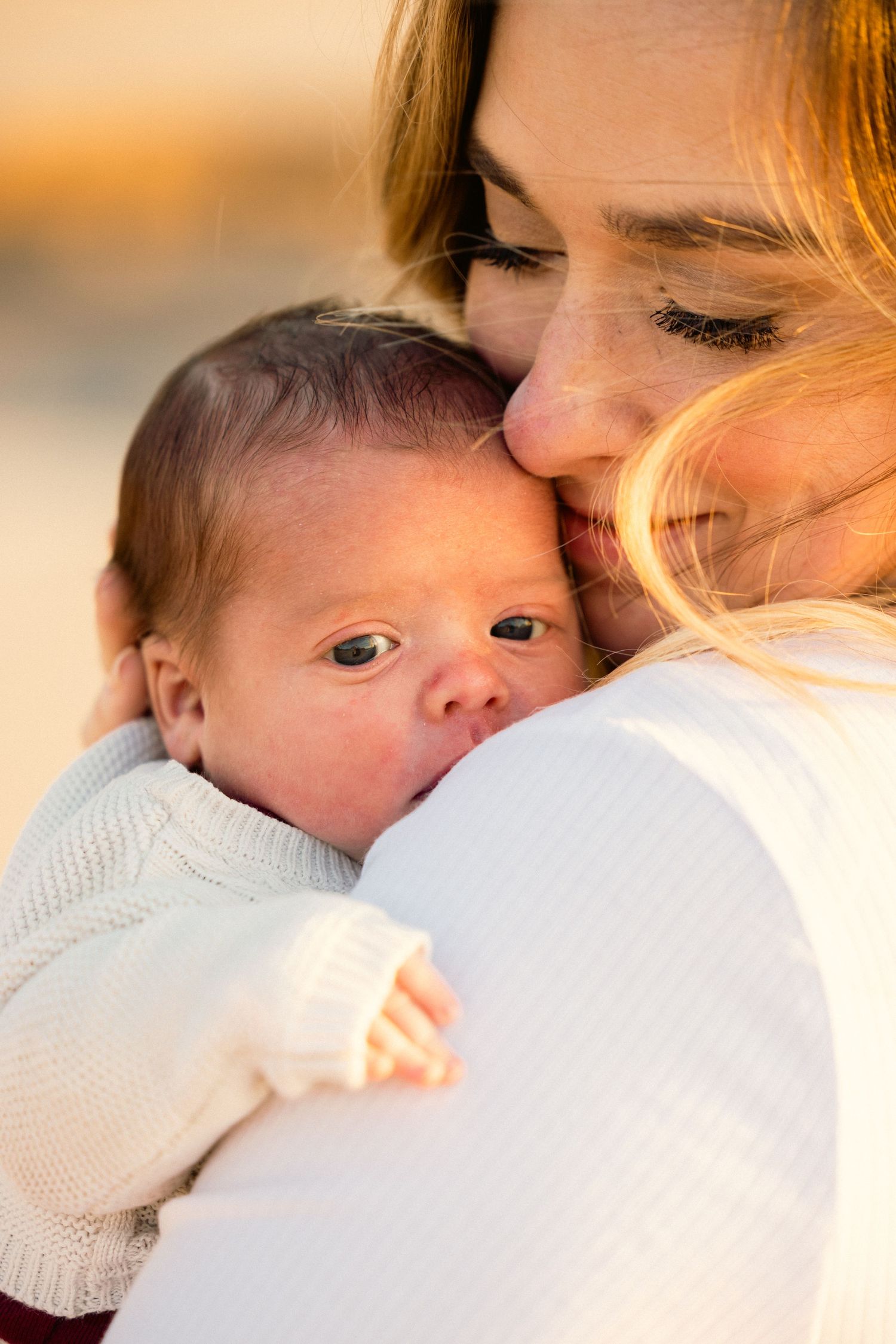 Tender moment between parent and infant in warm sunset lighting.