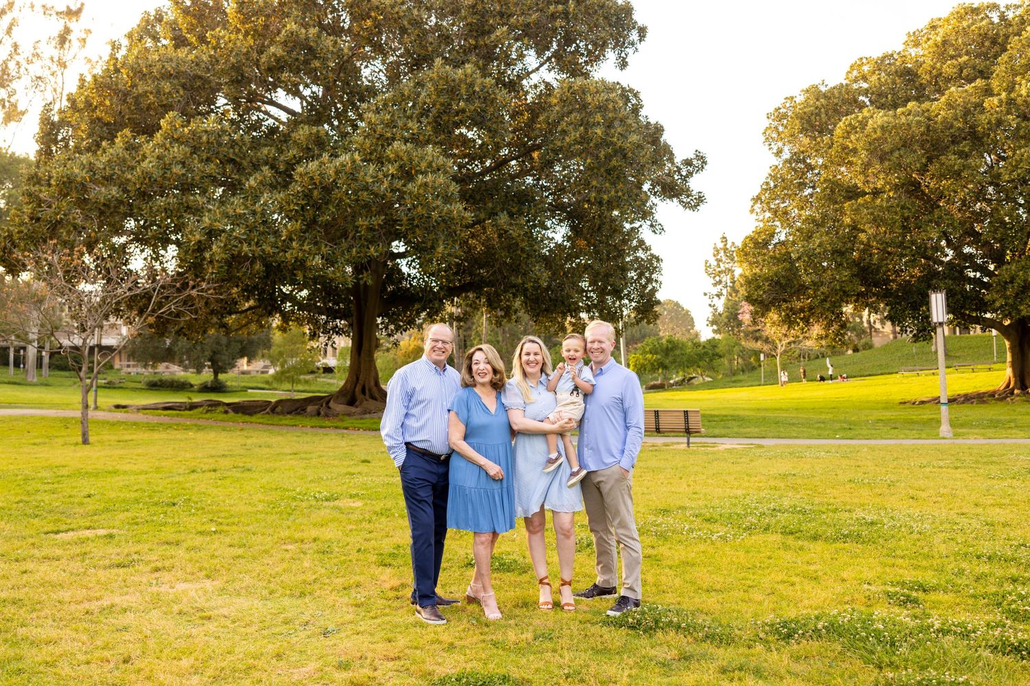 Family group wearing coordinated blue outfits poses in a grassy park.