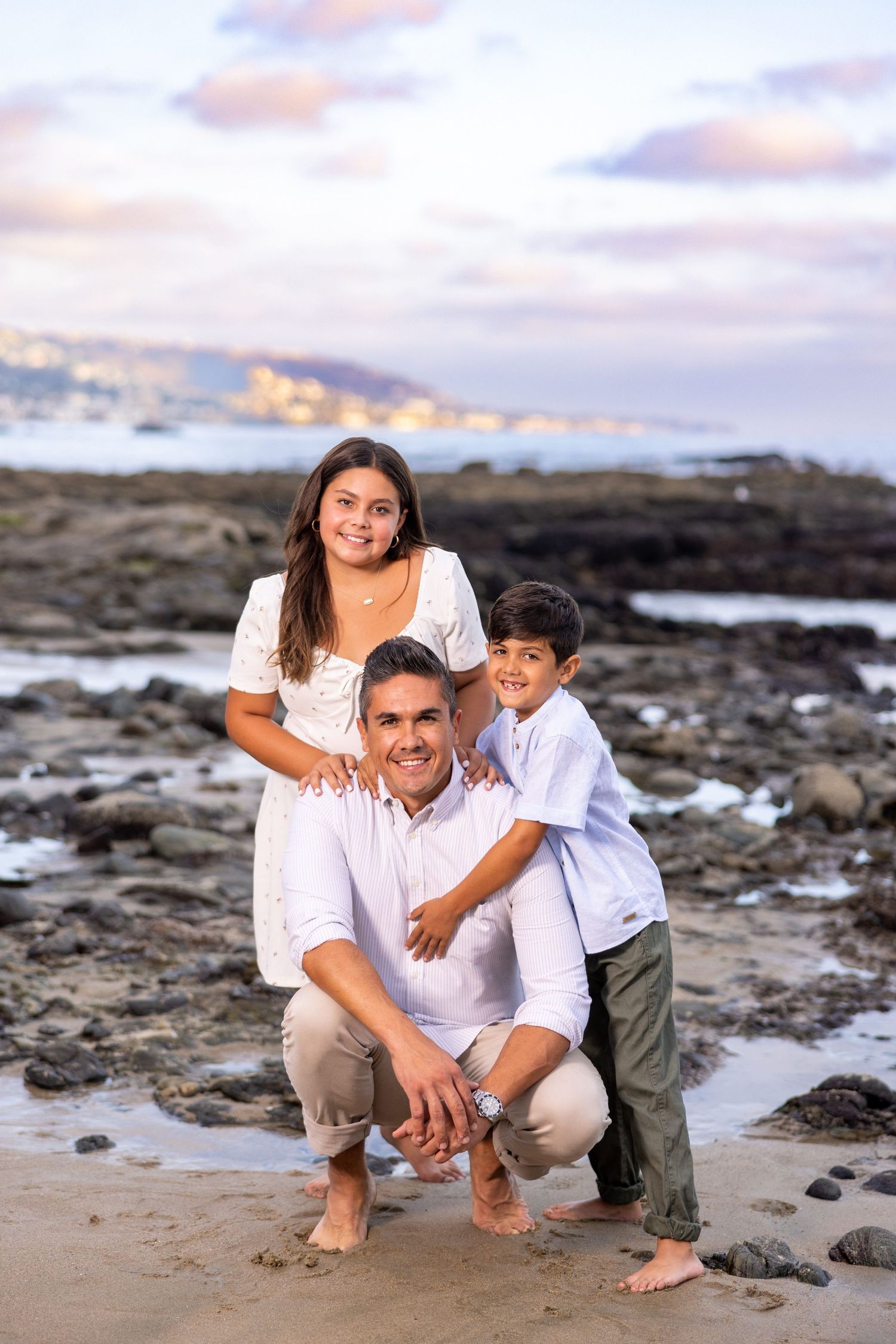 Family posing together on rocky beach shore at sunset.
