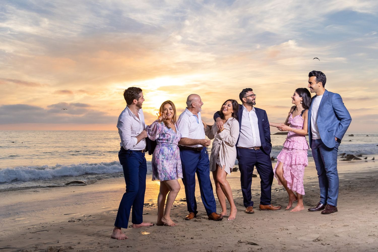 Casual group gathering on beach with sunset lighting and ocean waves in background.