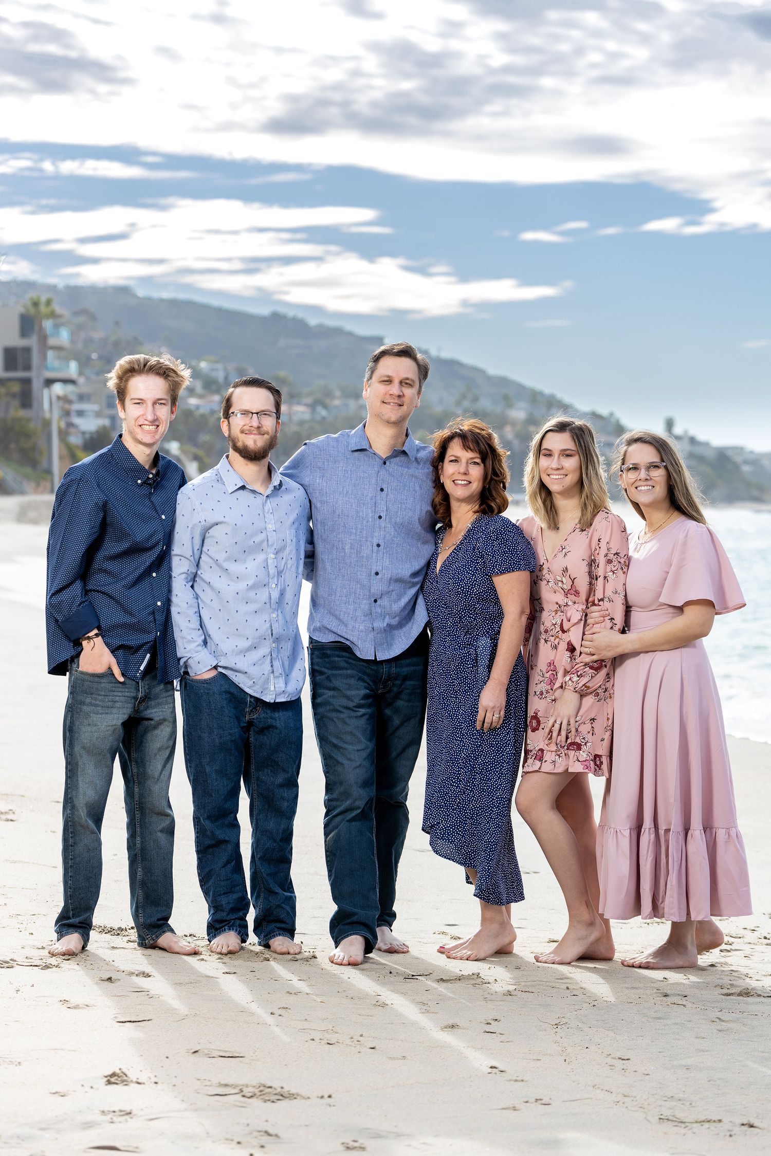 Family group standing together on beach with mountains and blue sky in background.