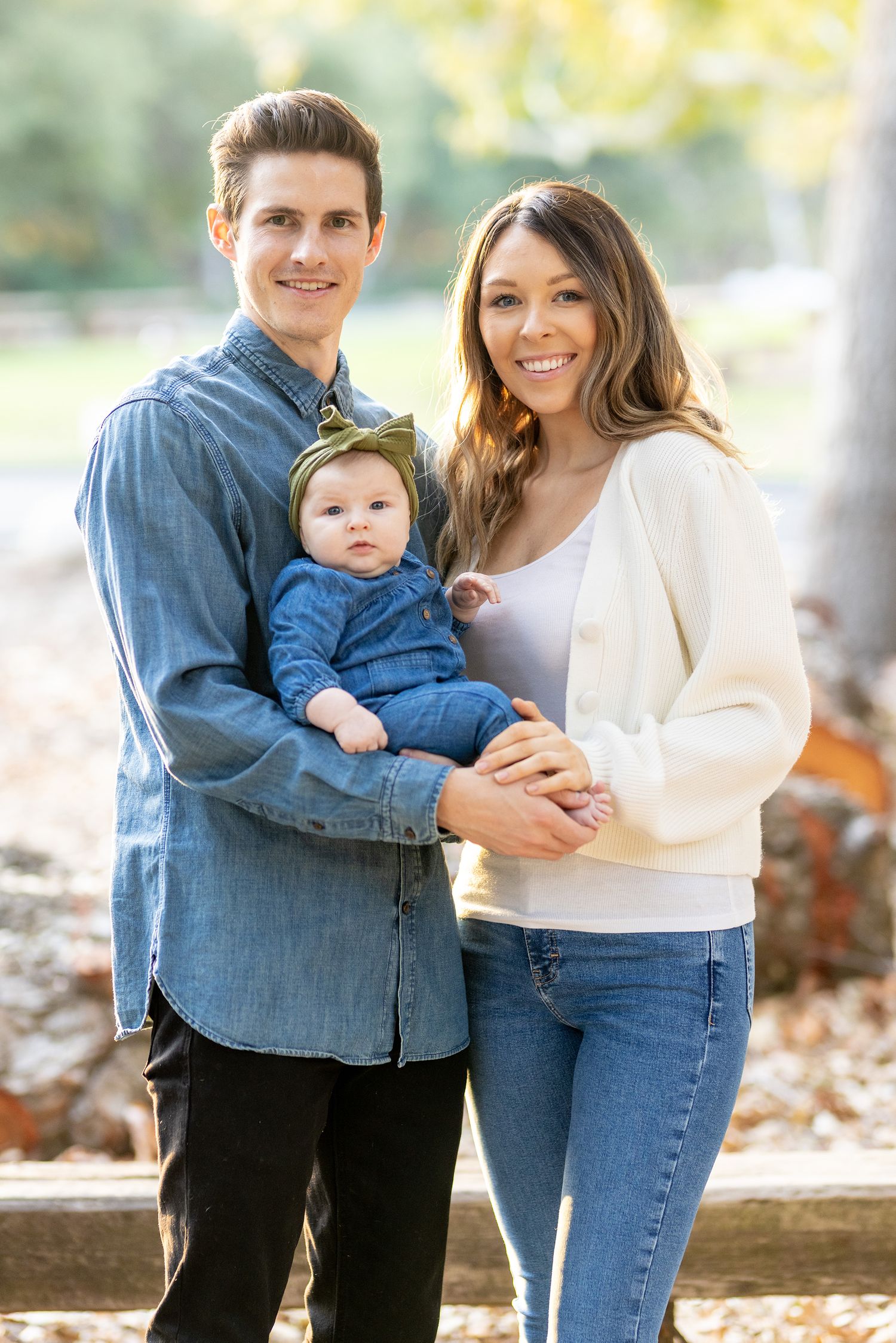 Family with baby in casual outfits pose outdoors in natural setting.