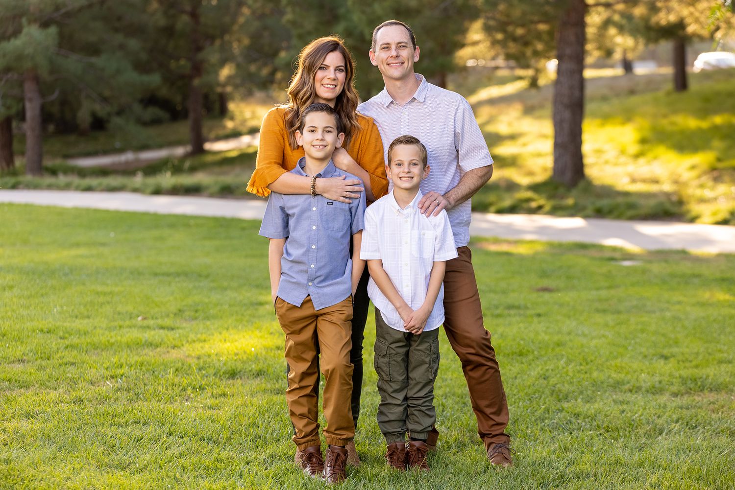 Family of four poses together on grassy lawn during warm sunset lighting.