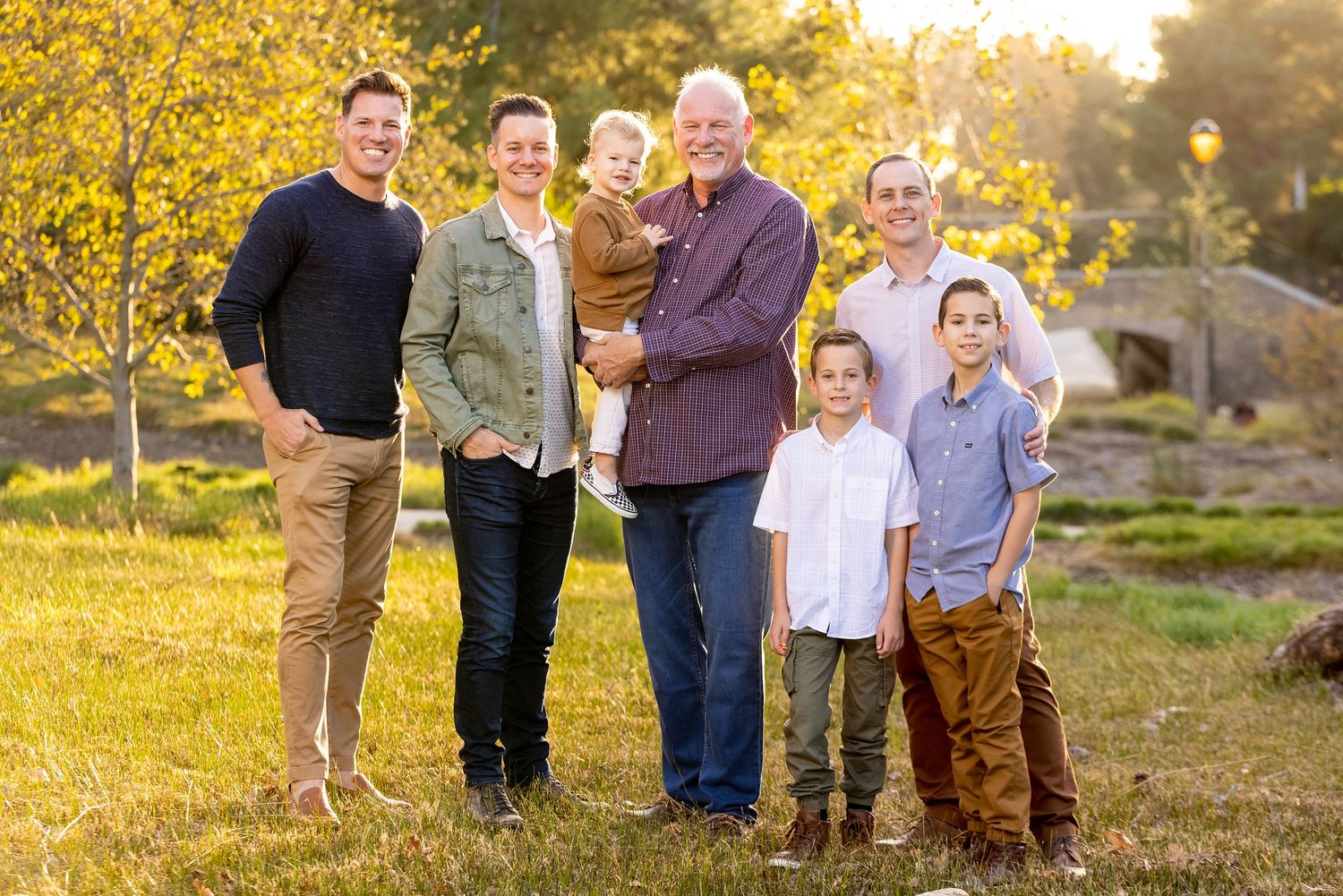 Multi-generational family group poses together against golden autumn scenery.