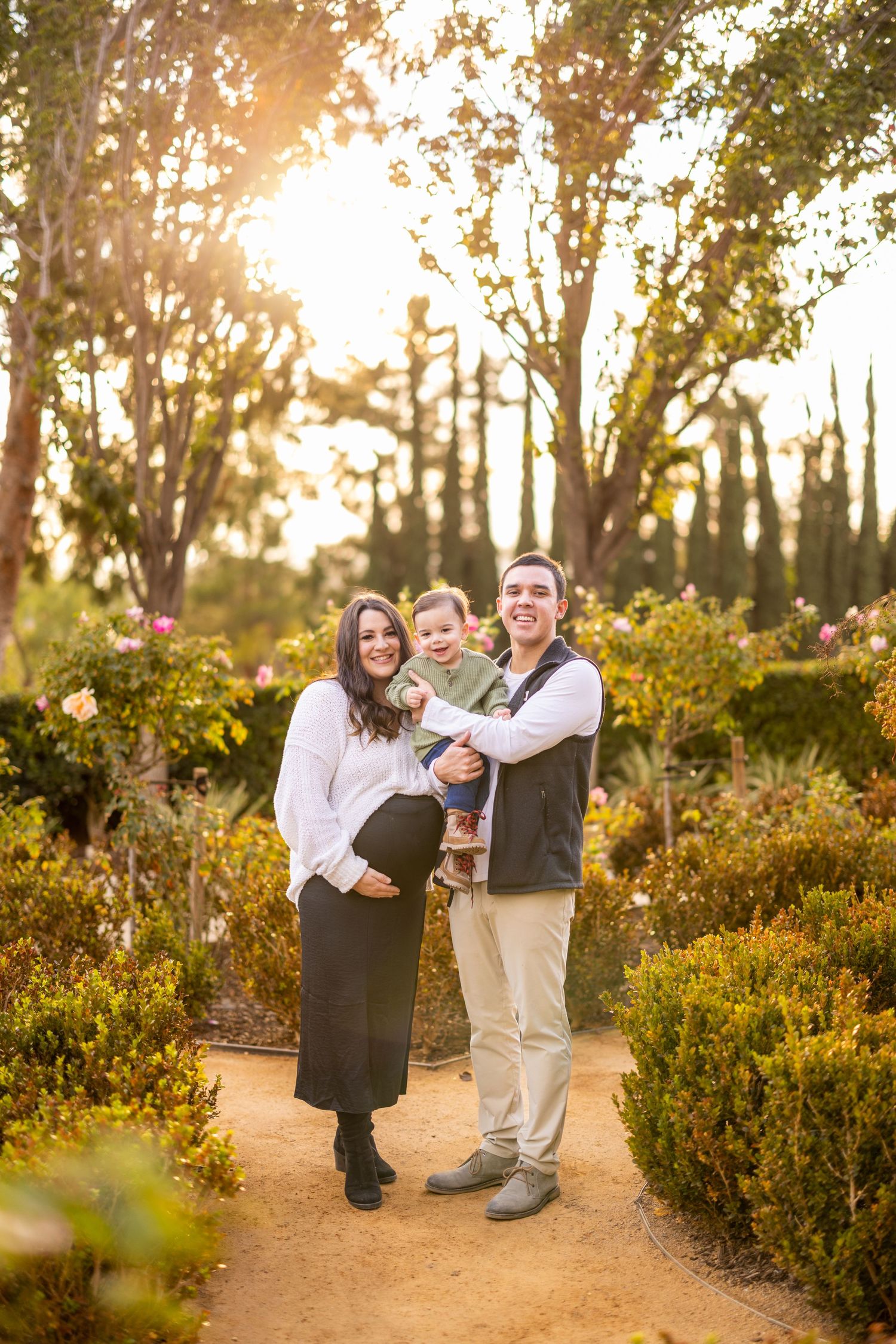 Family portrait with golden sunset light filtering through trees in garden setting.