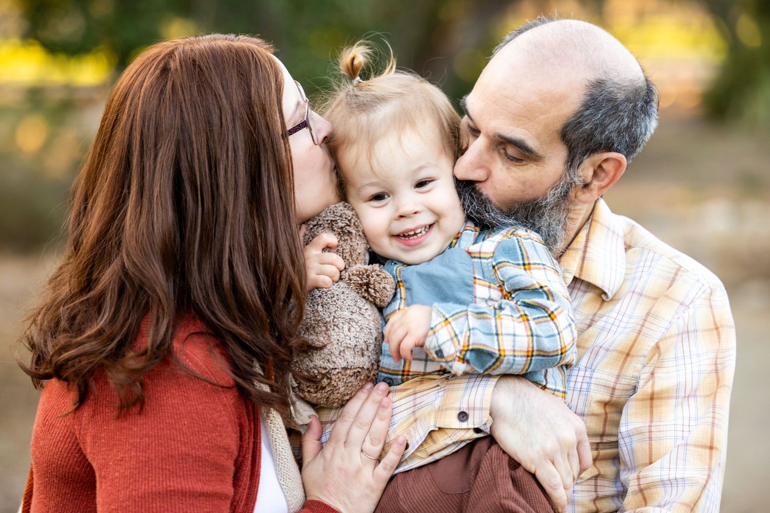 Parents sharing loving kisses with their smiling toddler.