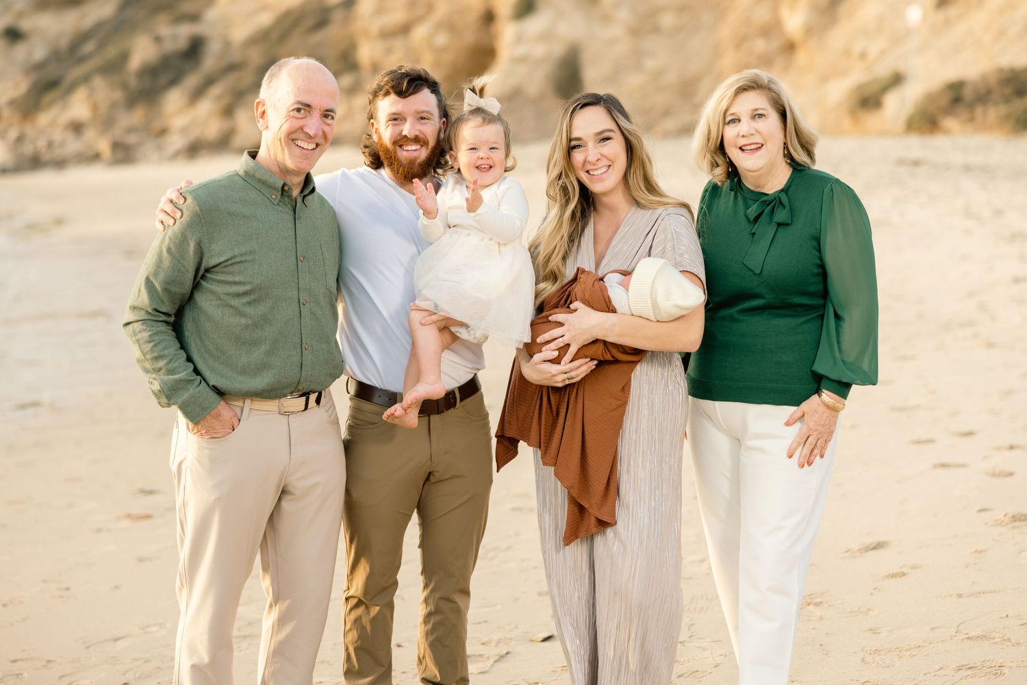 Group portrait of family members in coordinated casual attire on beach at sunset.