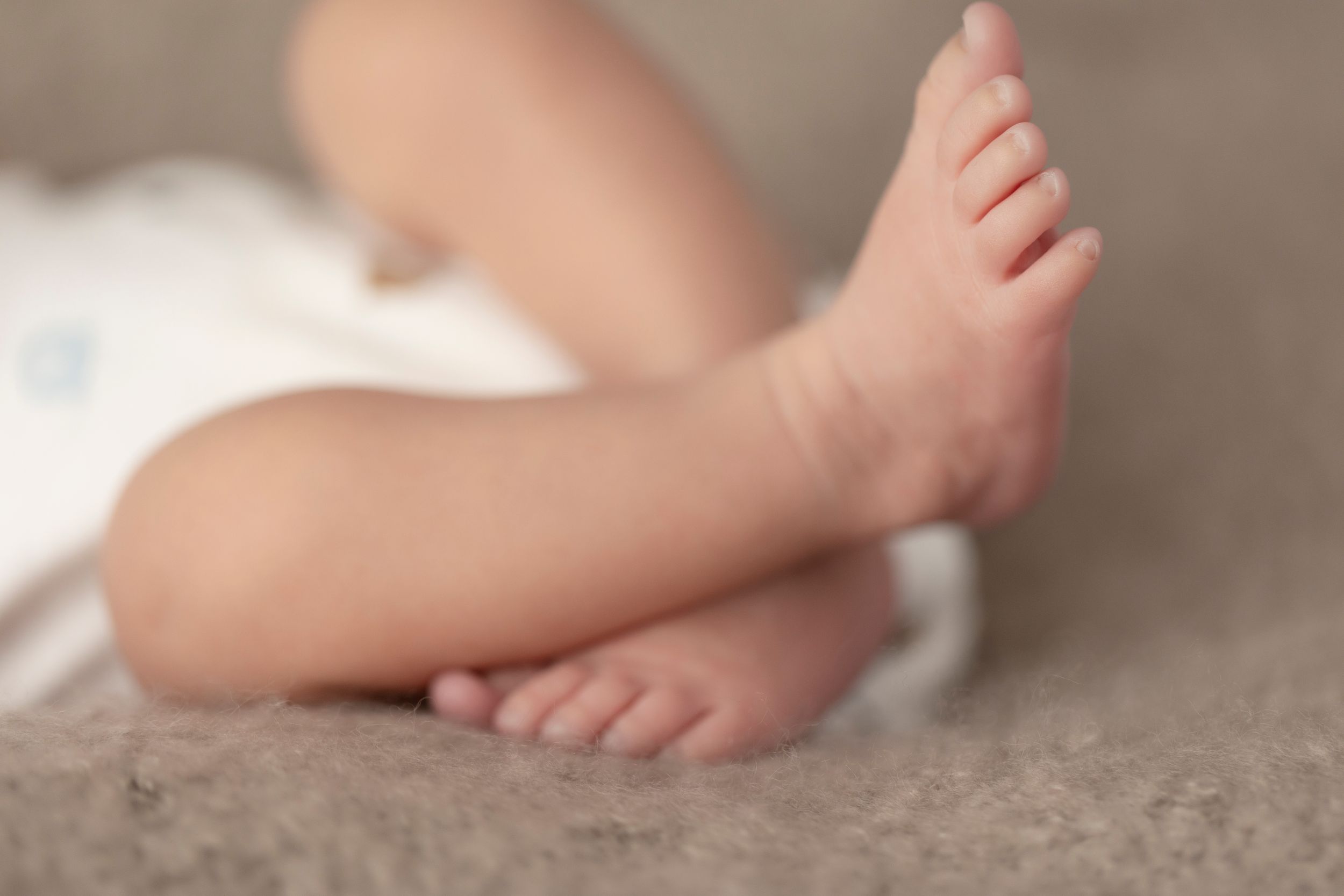 Close-up of tiny baby feet and toes on neutral beige background.