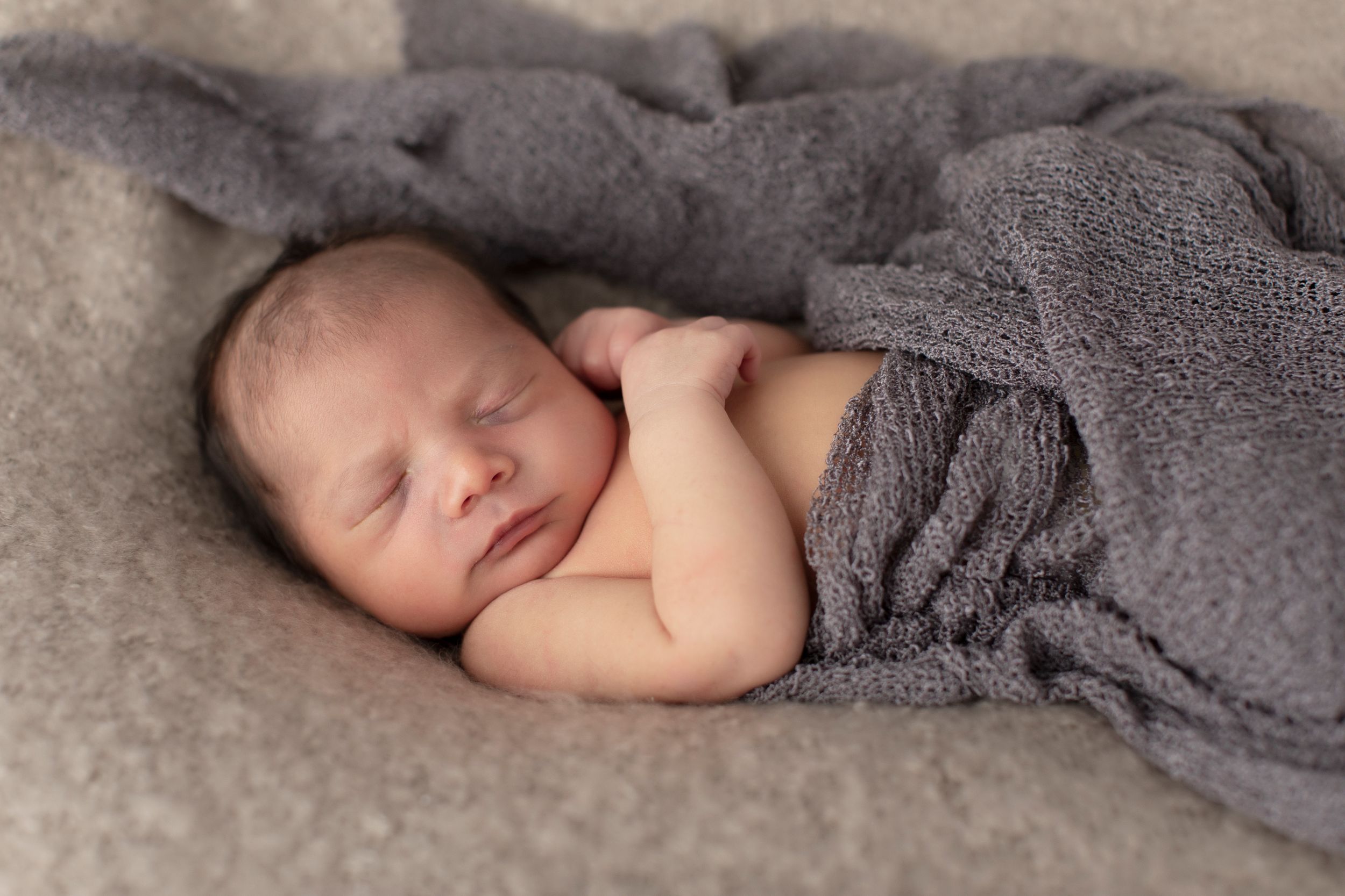 Newborn baby wrapped in gray blanket sleeping peacefully during photo session.