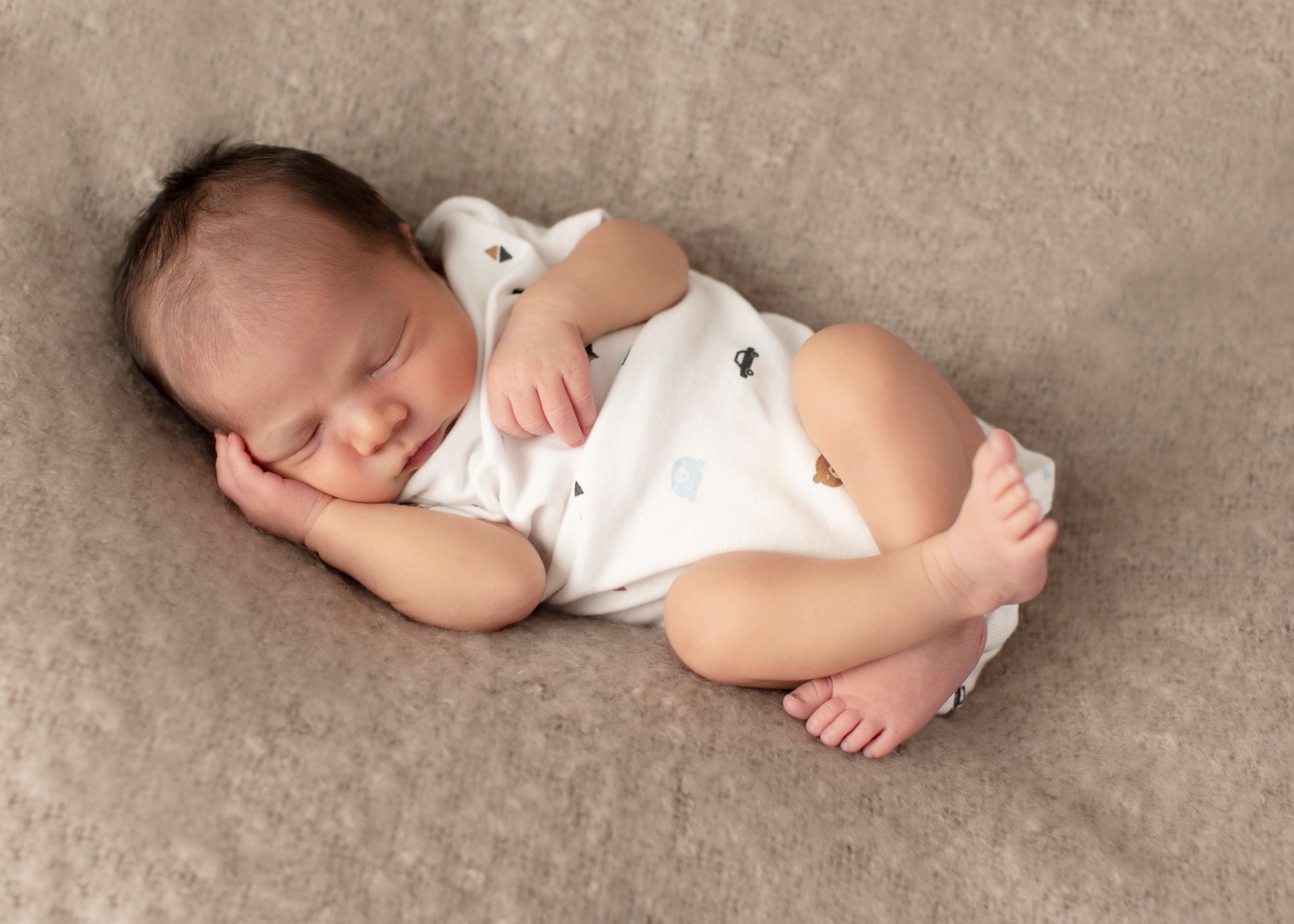 Peaceful newborn baby resting on soft beige blanket during professional photo session.