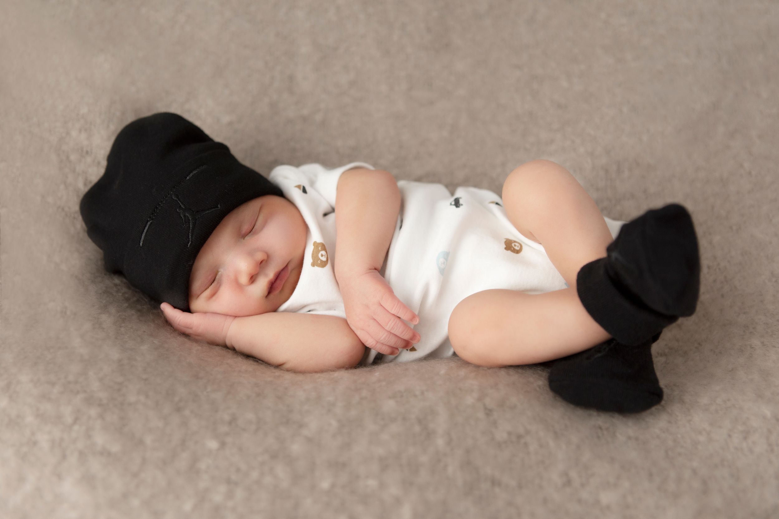 Sleeping baby in white onesie lying on beige carpet during newborn photoshoot.