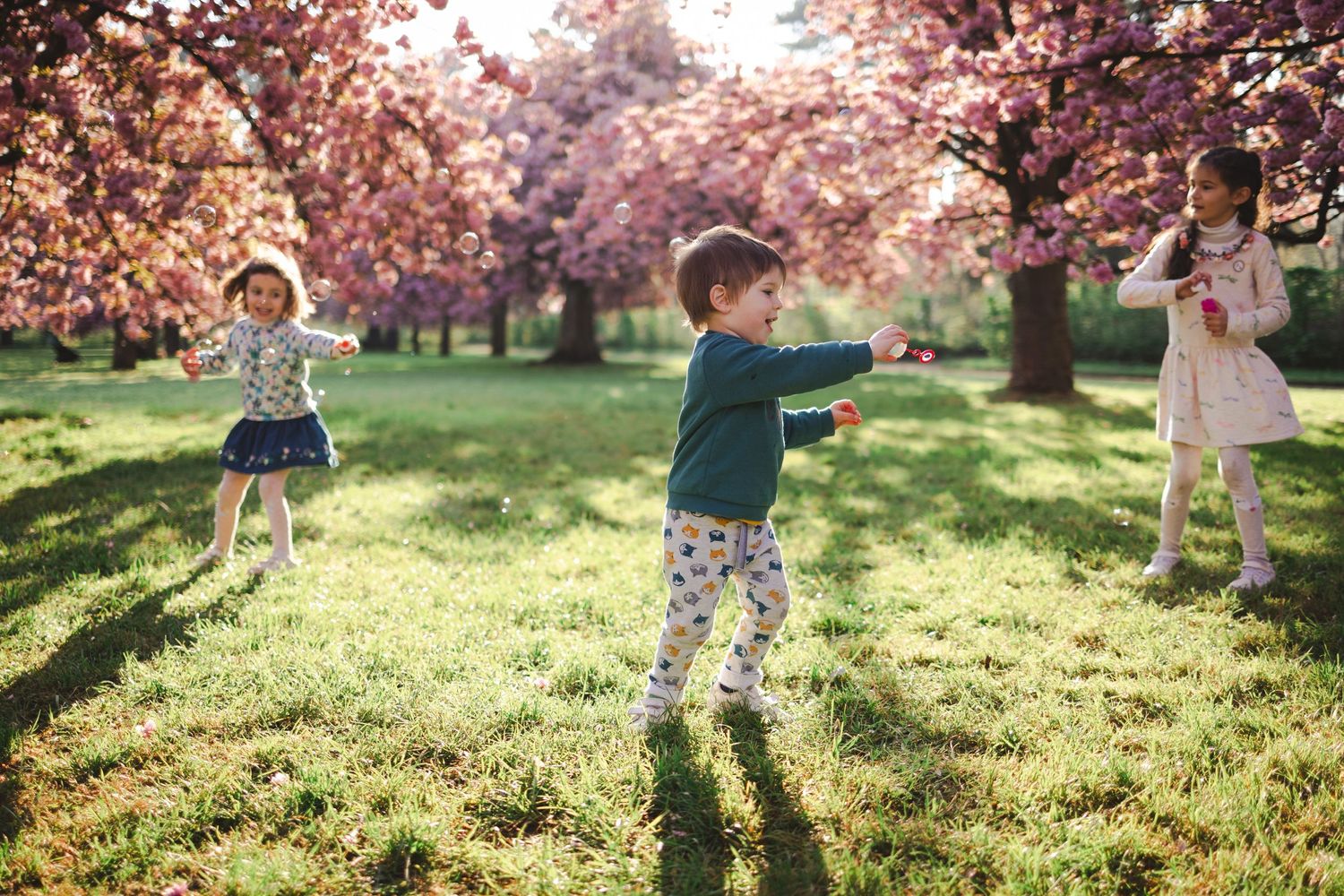 Trois enfants en tenues pastel jouent à l'occasion d'un shooting photo sous des arbres en fleurs