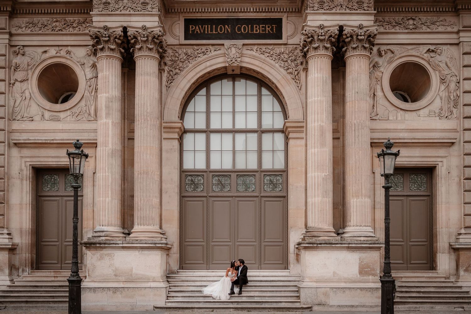 A newlywed couple sit and share a moment together on the steps of the Louvre, Paris