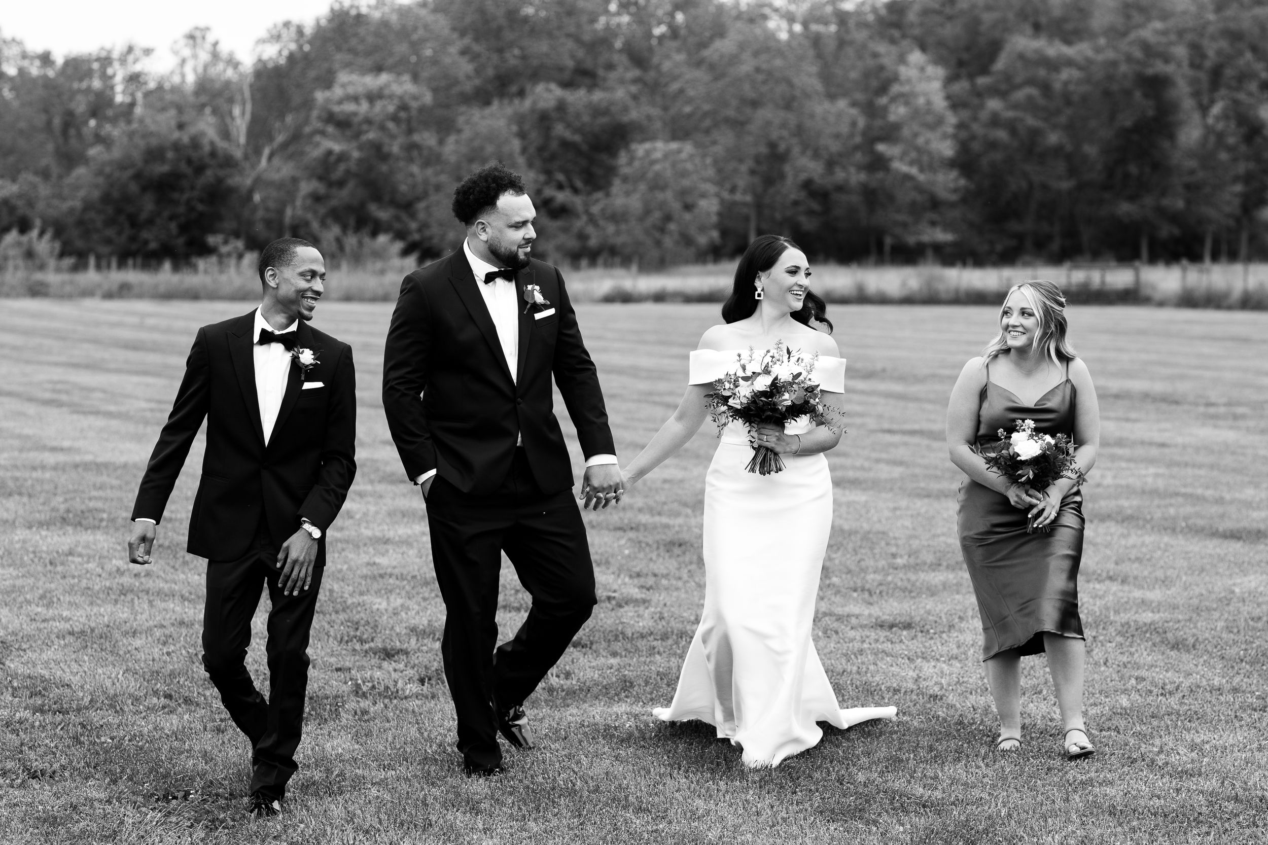 Black and white candid wedding party walking across field.