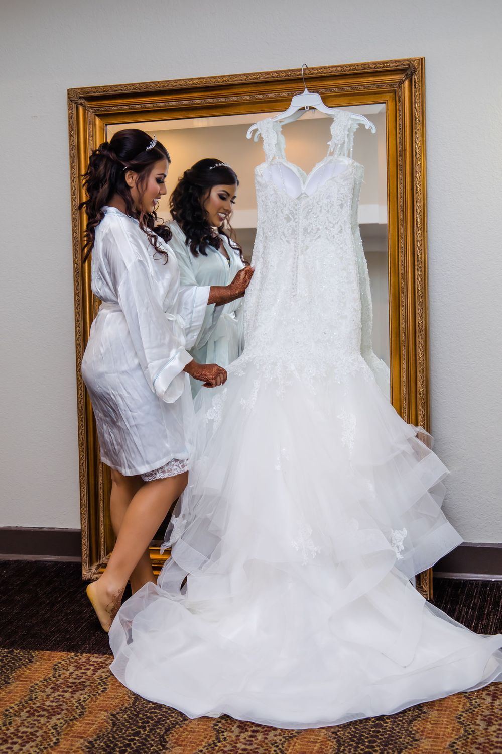 Elegant white wedding dress hanging on display in front of a gold-framed mirror.