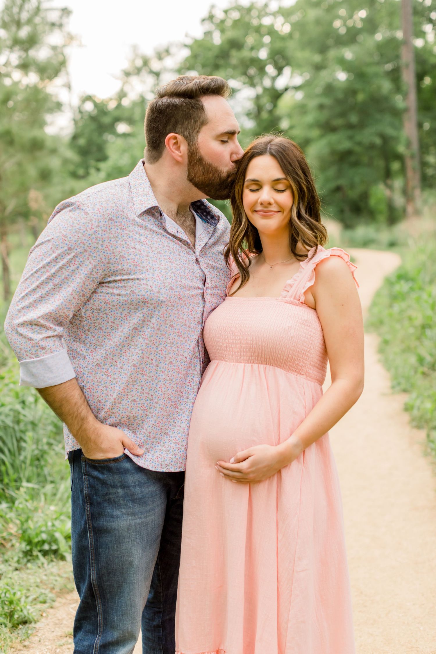A sweet intimate moment between an expectant couple on a sunlit nature trail.