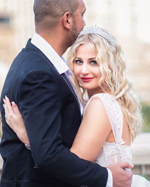 Romantic wedding portrait with elegant white gown and formal attire against classic architecture.