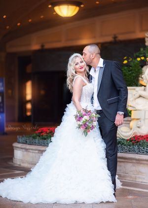 Elegant couple in wedding attire sharing romantic moment by floral garden entrance.