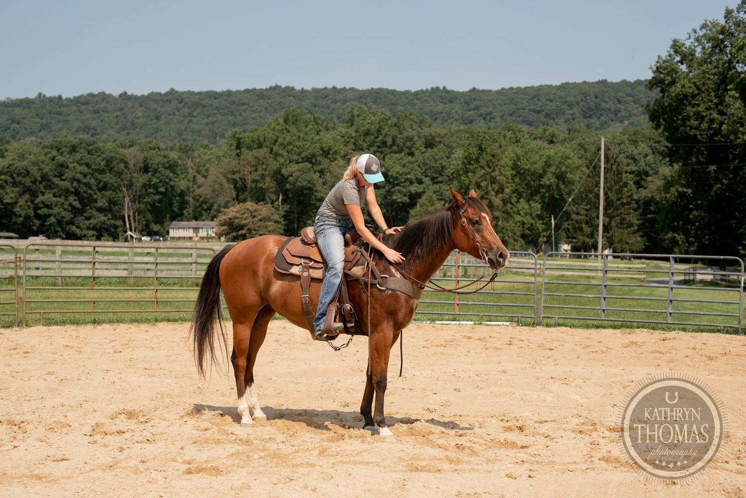 A rider on horseback practices in a sandy outdoor arena surrounded by wooden fencing and trees.