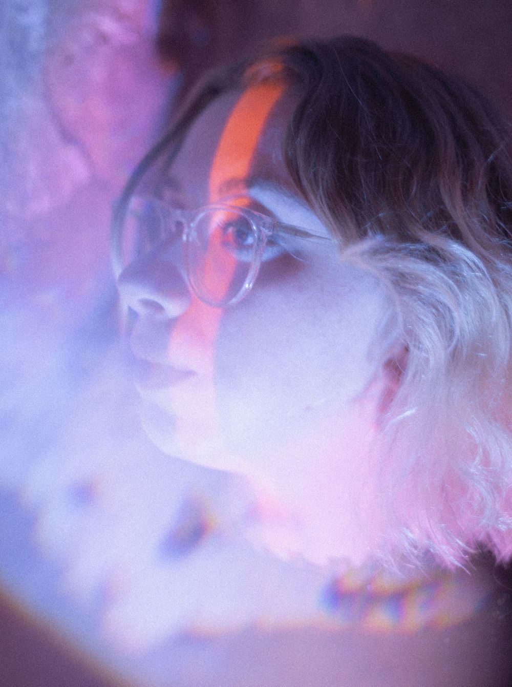 An artistic portrait with neon lighting and glasses creating a dreamy atmosphere.