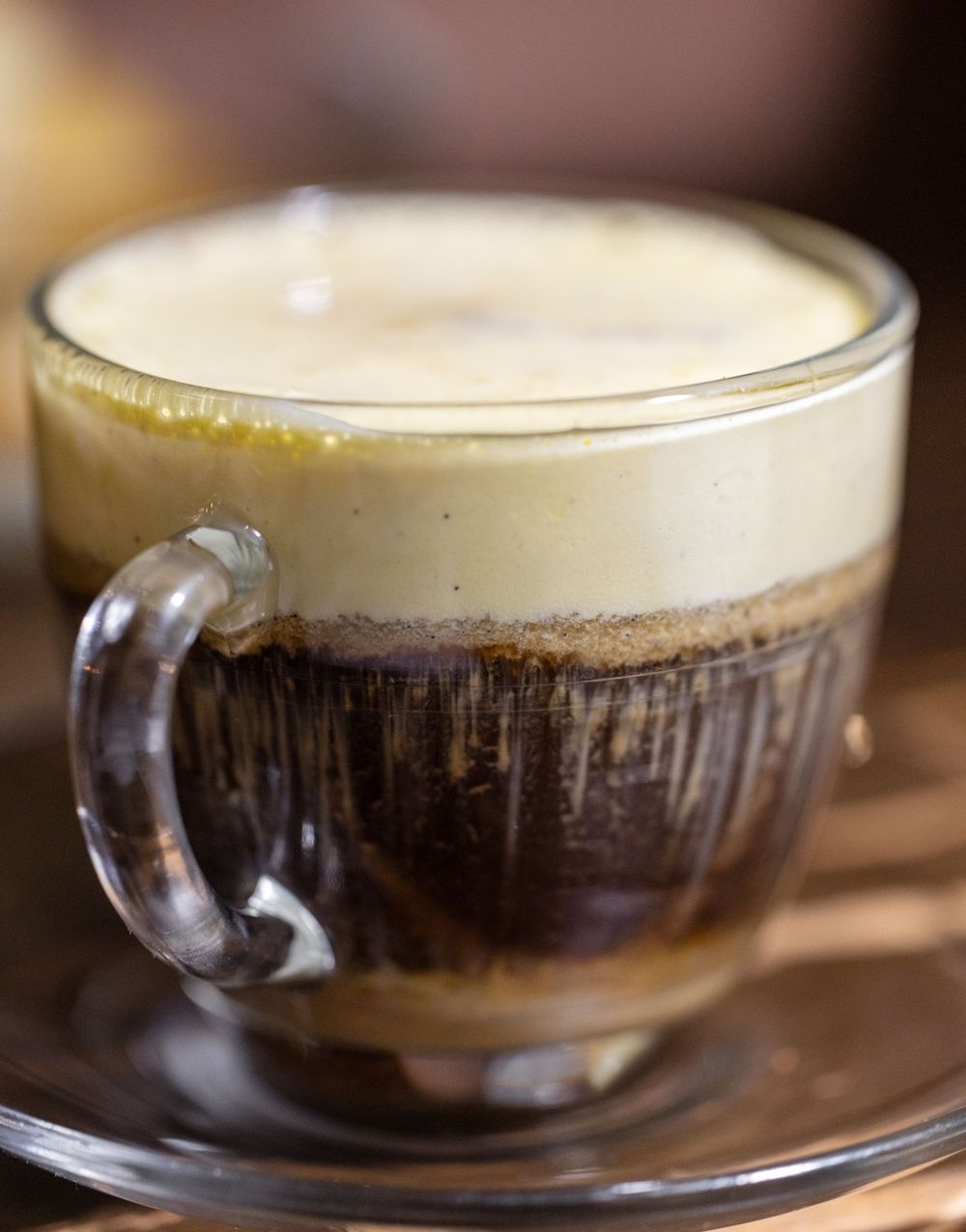 A layered coffee drink with creamy foam top served in a clear glass mug.