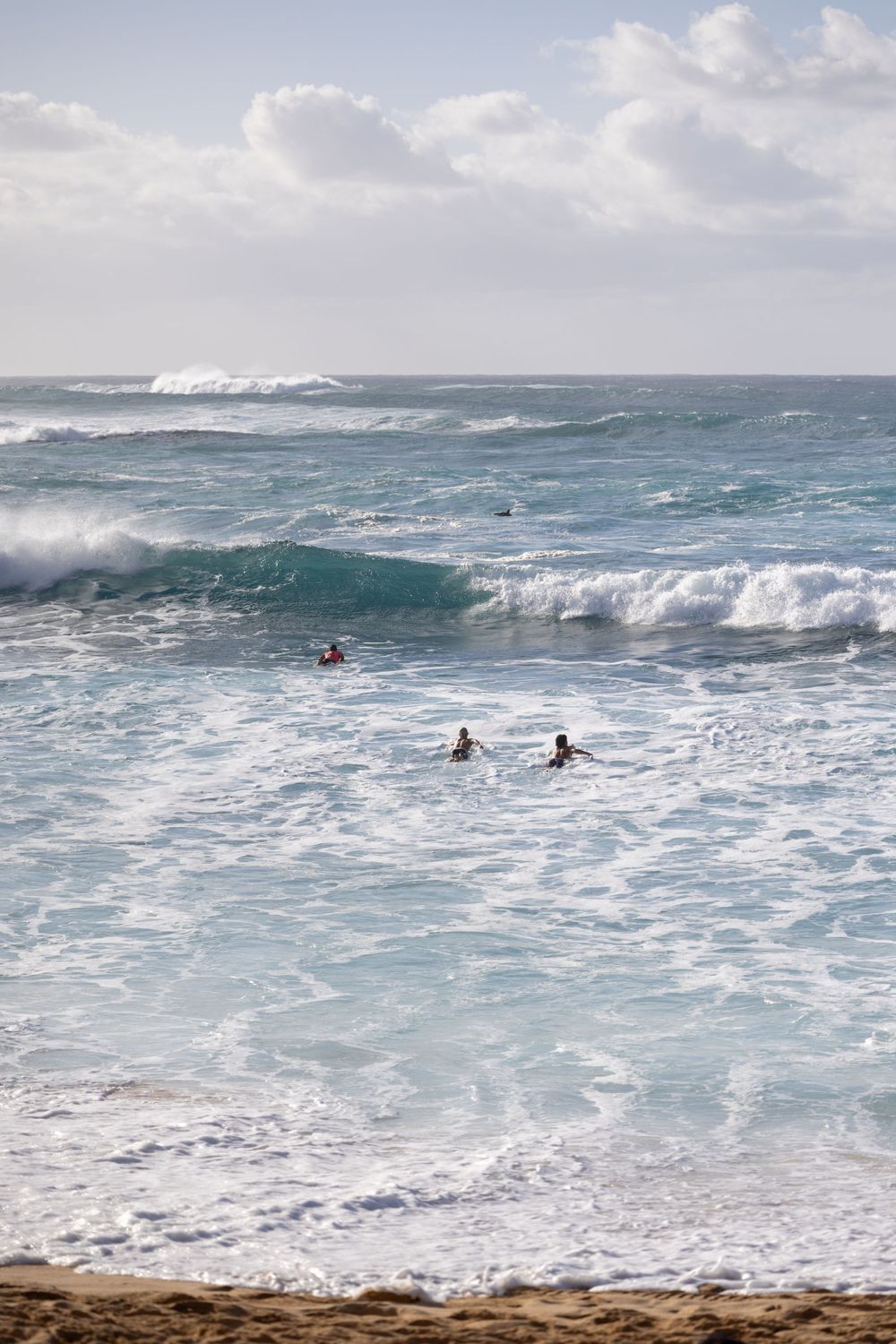 Surfers navigate large waves in a stormy ocean with white-capped swells.