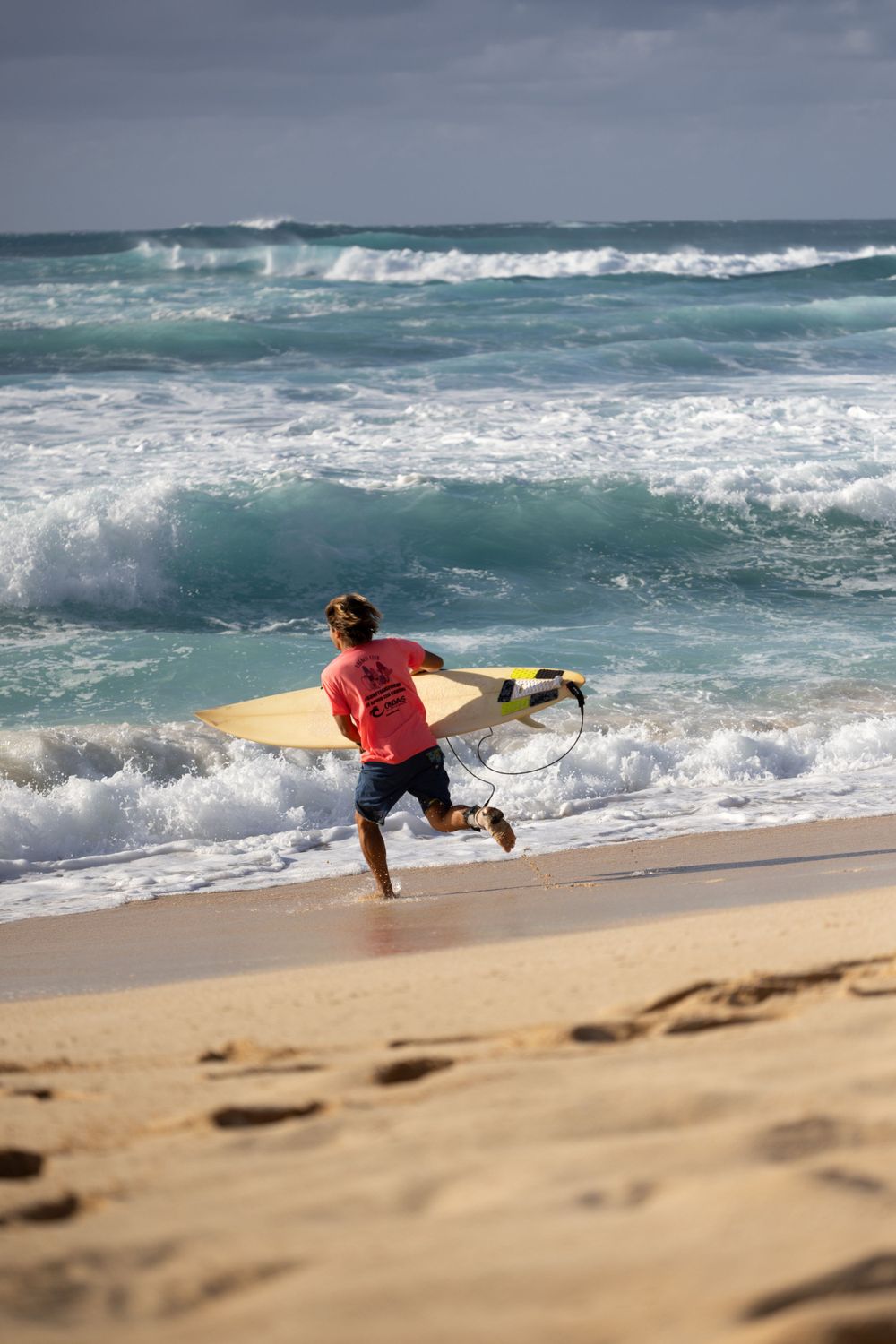 Surfer running into ocean waves with yellow surfboard on sandy beach.