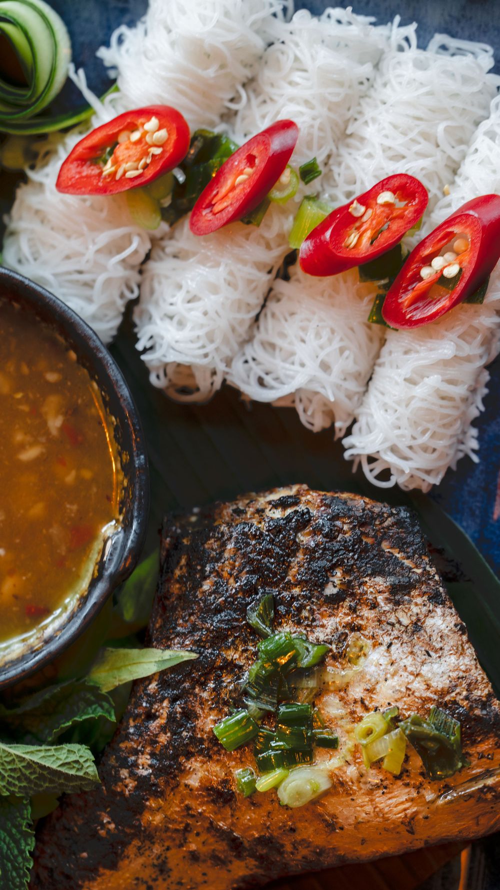 Fresh rice noodles topped with sliced red chili peppers served alongside grilled fish and dipping sauce.