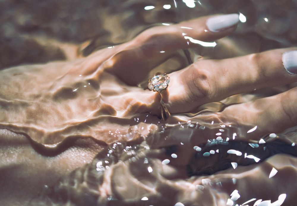 Hands touching water surface creating ripple effects in warm sunlight.