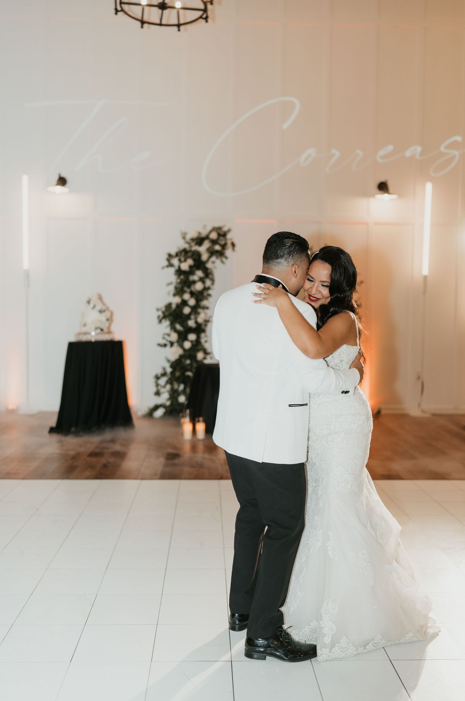 A romantic first dance moment between newlyweds in an elegant white venue with modern lighting.