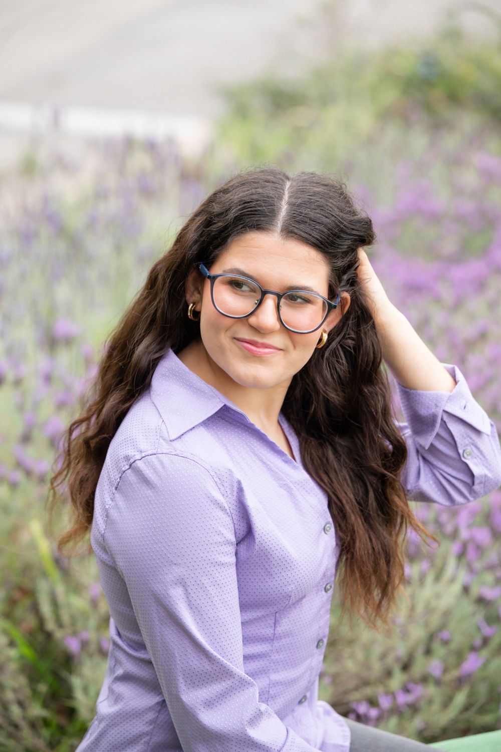 Portrait in a purple shirt with glasses against lavender flowers in a garden setting.