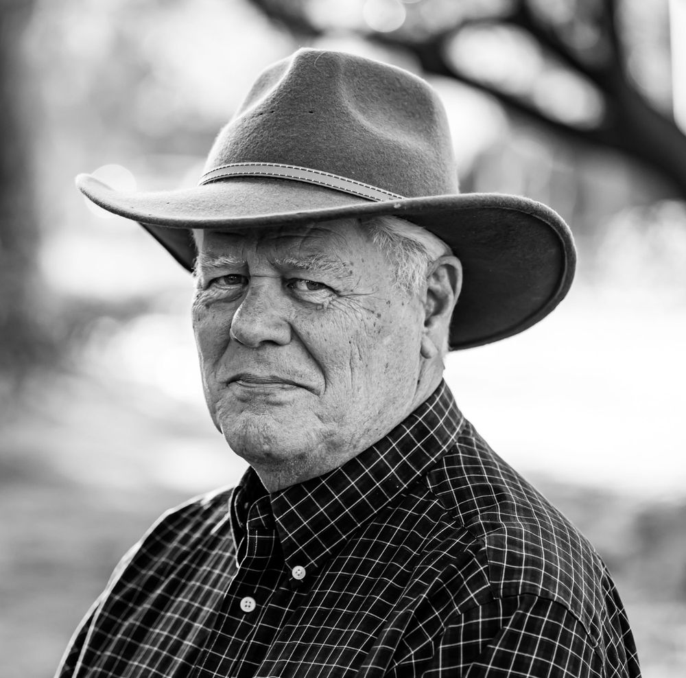 Black and white portrait of senior man wearing cowboy hat and plaid shirt.