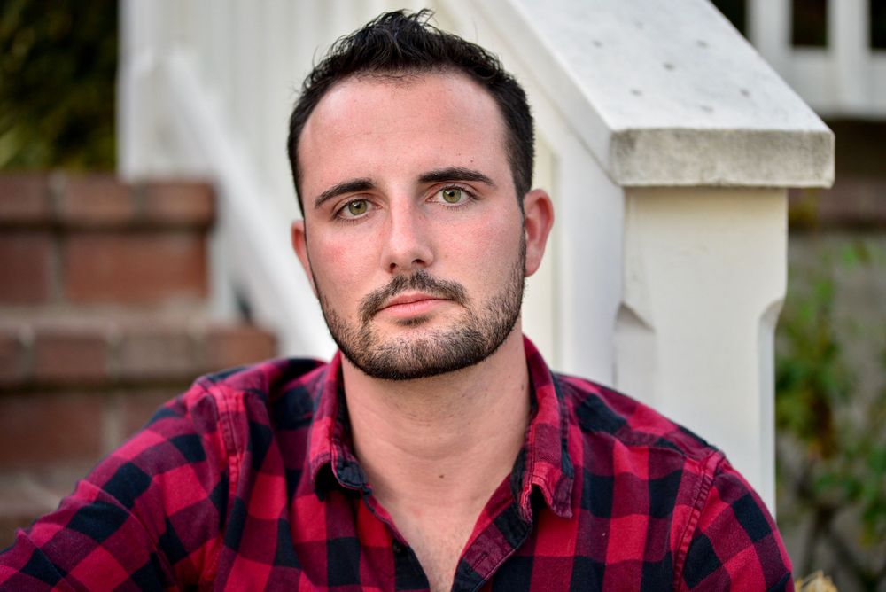 Portrait shot of person wearing red and black buffalo plaid flannel shirt against light background.