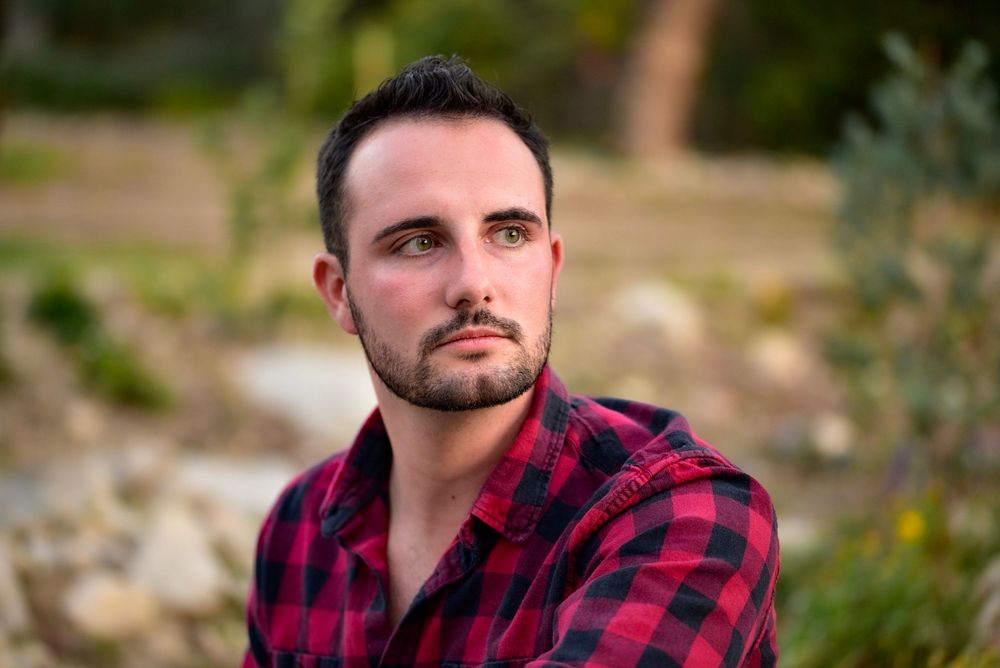 Outdoor portrait of person in red plaid shirt with natural lighting and blurred background.
