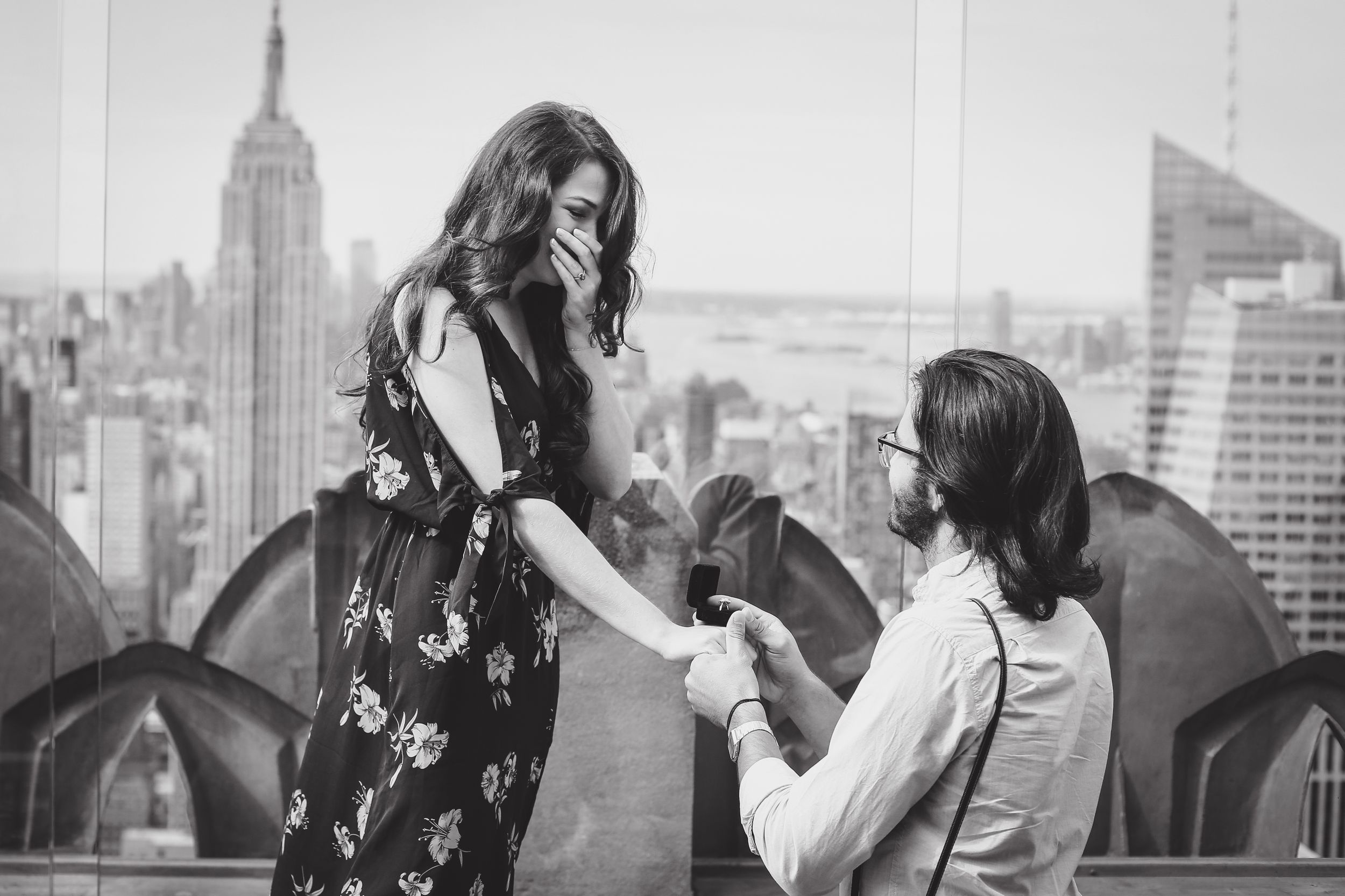Black and white engagement moment captured on NYC rooftop with Empire State Building visible.