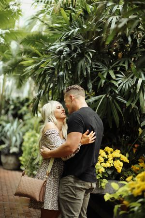 Romantic couple embracing in a lush tropical garden setting with yellow flowers.