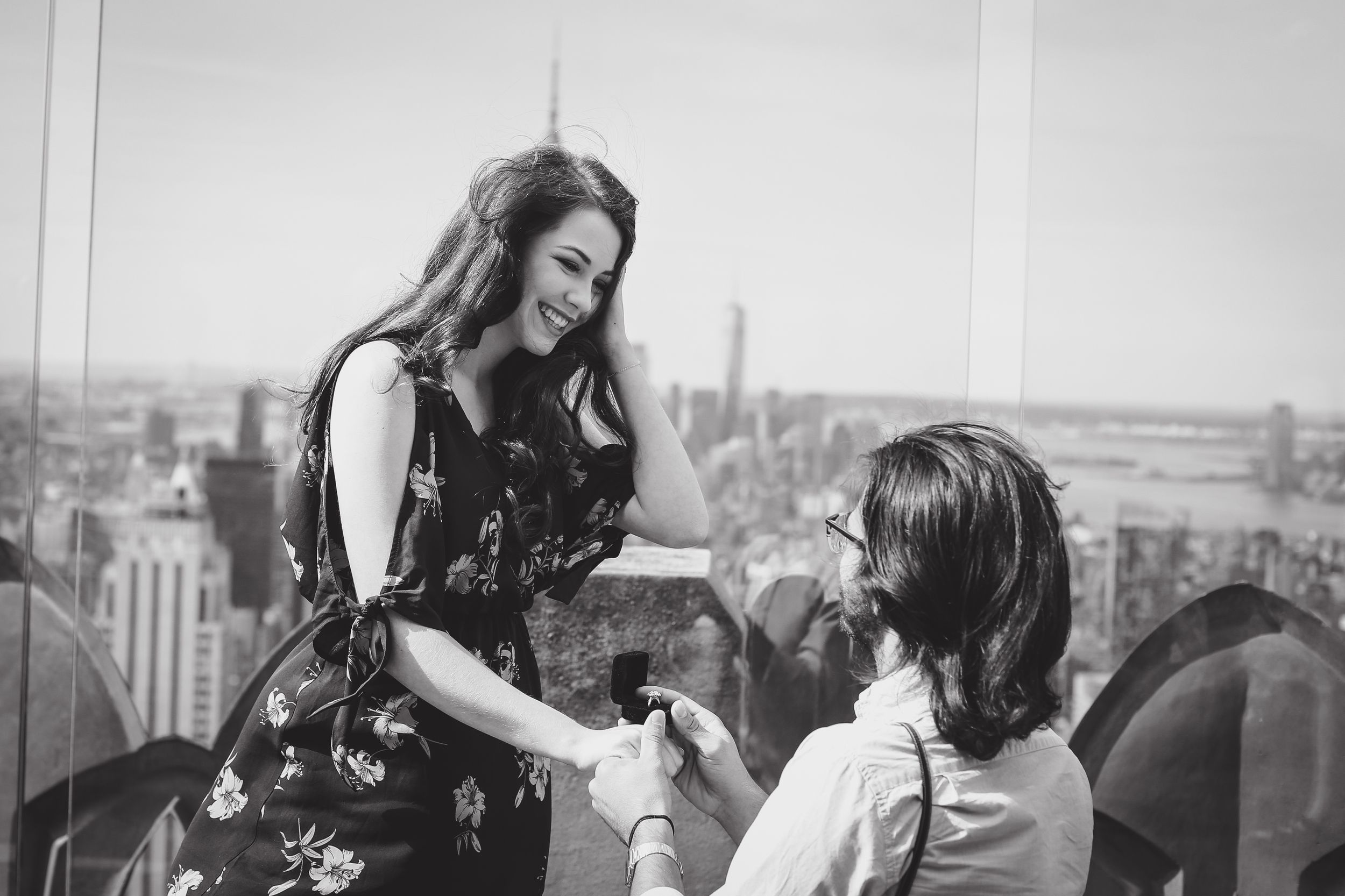 Black and white rooftop proposal scene with city skyline backdrop.