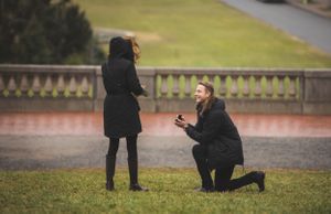 A romantic proposal scene with one person kneeling on wet grass.