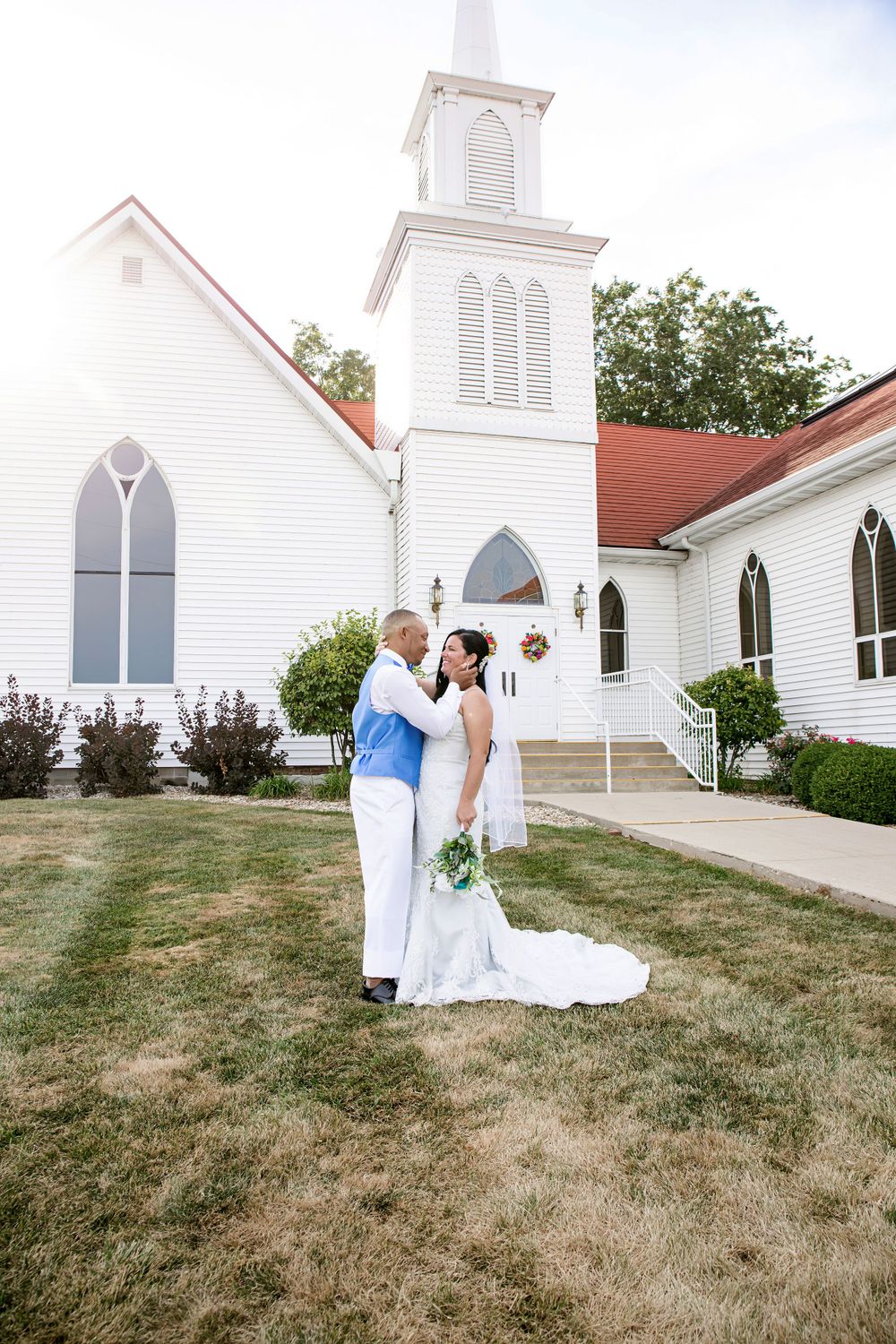 A romantic wedding portrait taken outside a classic white country church with tall steeple.