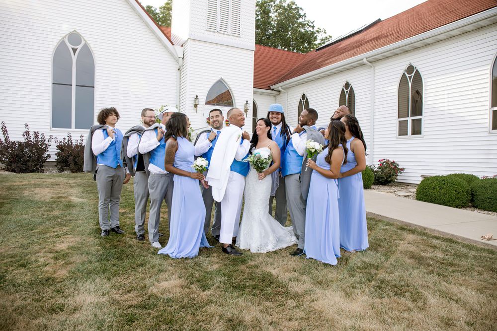 Wedding party wearing blue and grey poses together outside traditional white church.