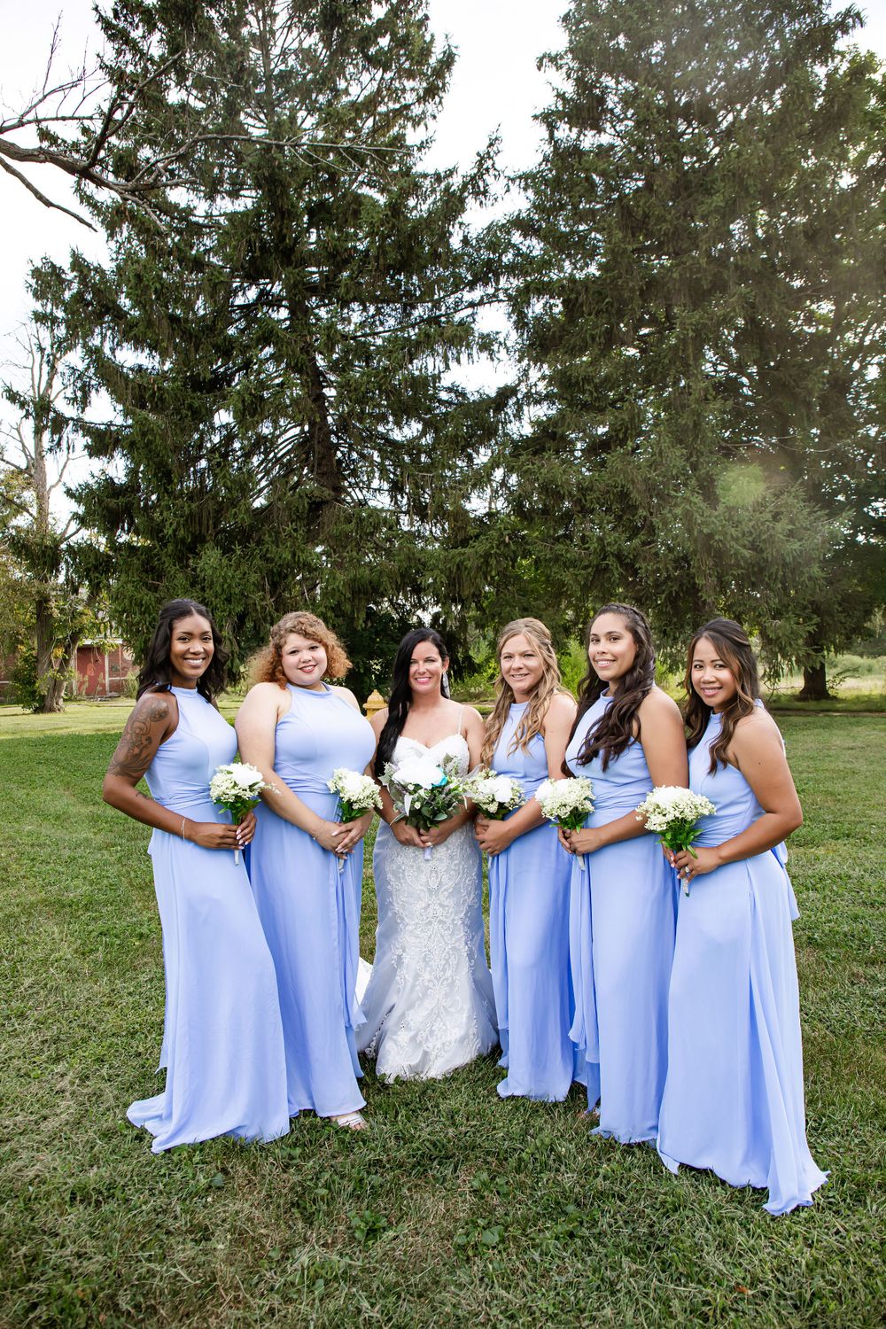 Bridesmaids in flowing light blue dresses pose with bride on grassy lawn.