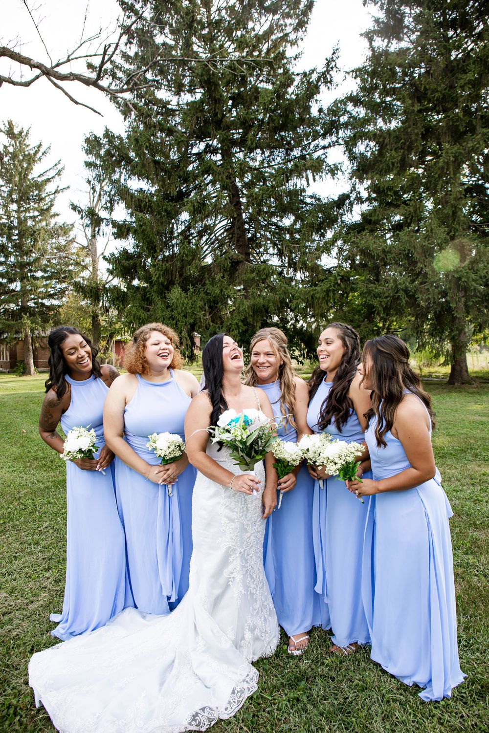 Candid moment of bridal party laughing together outdoors under evergreen trees.