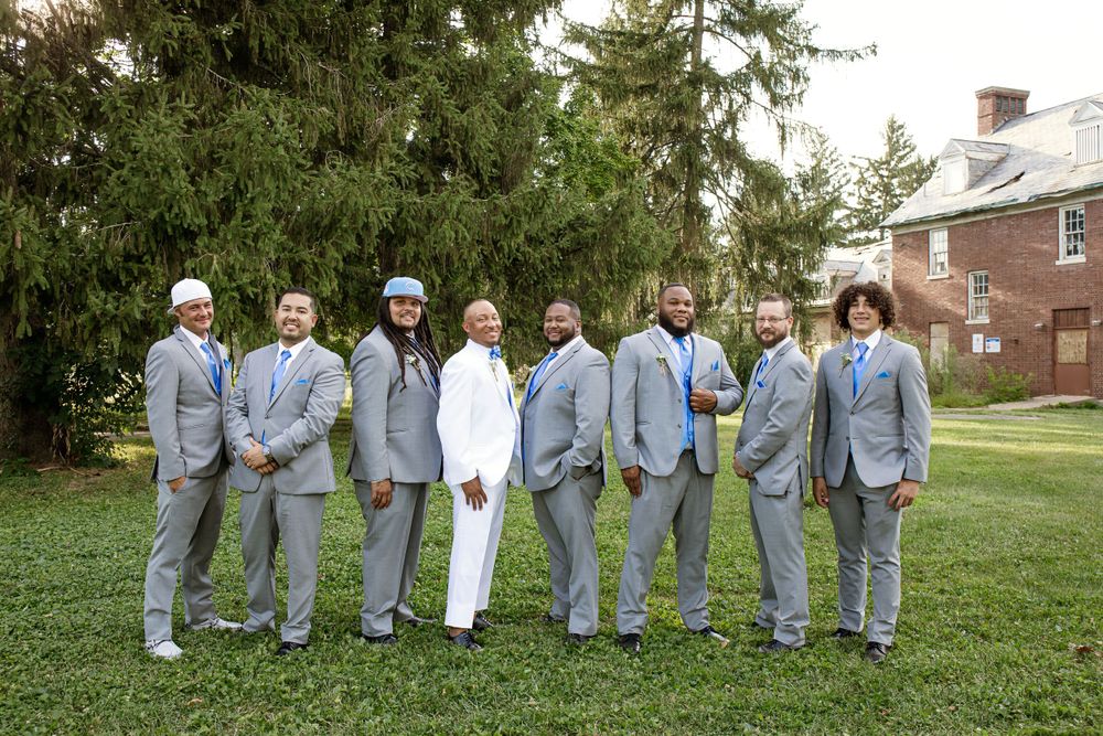 Groomsmen in coordinating grey suits pose together on lawn for formal wedding photo.