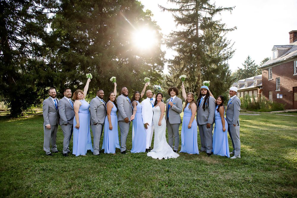 Full wedding party in blue and grey attire celebrates during sunset outdoor portrait.
