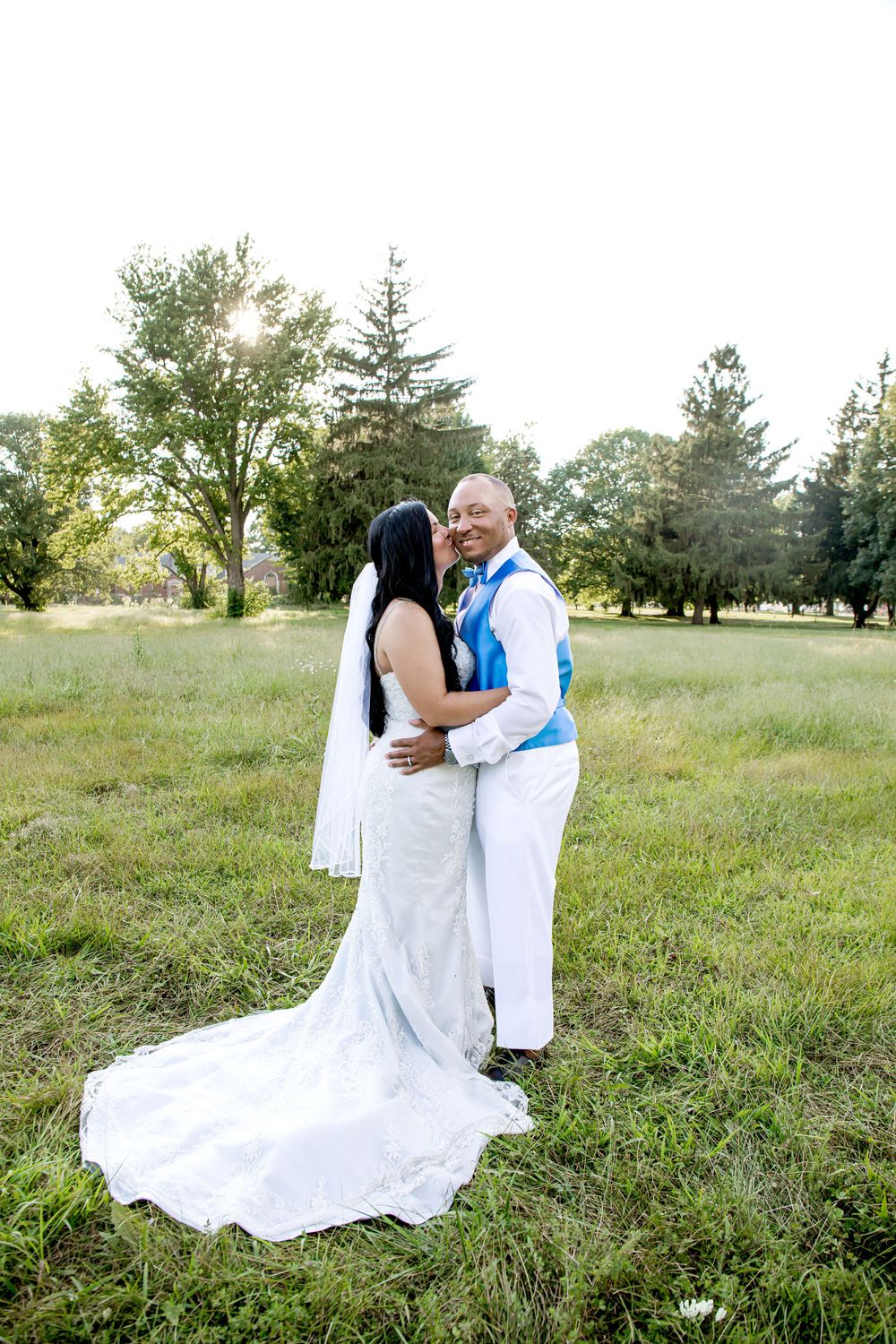 A romantic wedding moment captured outdoors with a flowing white dress and sunlit trees in the background.