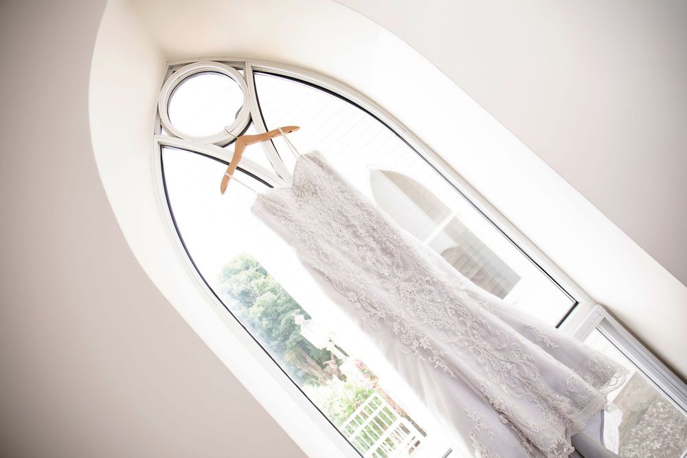 A wedding dress hangs in arched window frame creating elegant silhouette.