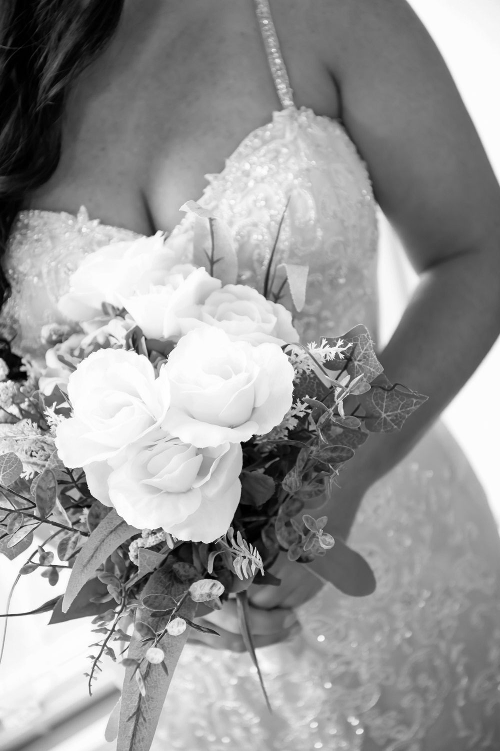 Close-up of a white rose wedding bouquet and lace wedding dress details in black and white.